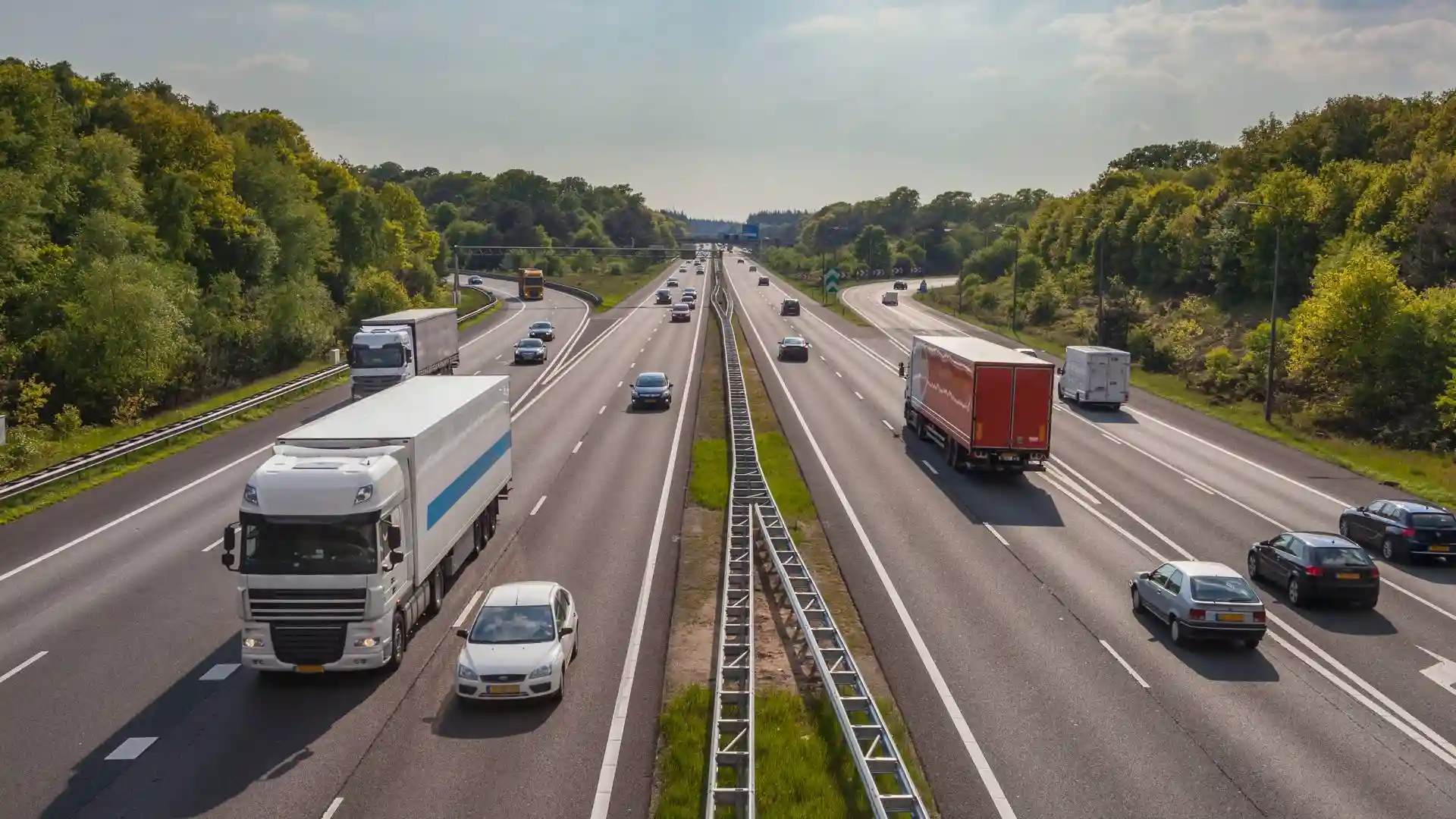 Multi-lane highway traffic surrounded by green trees.