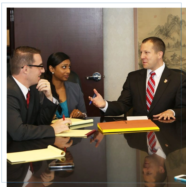 WHY-CHOOSE-THE-IRWIN-LAW-FIRM Three business people in suits discussing at a table